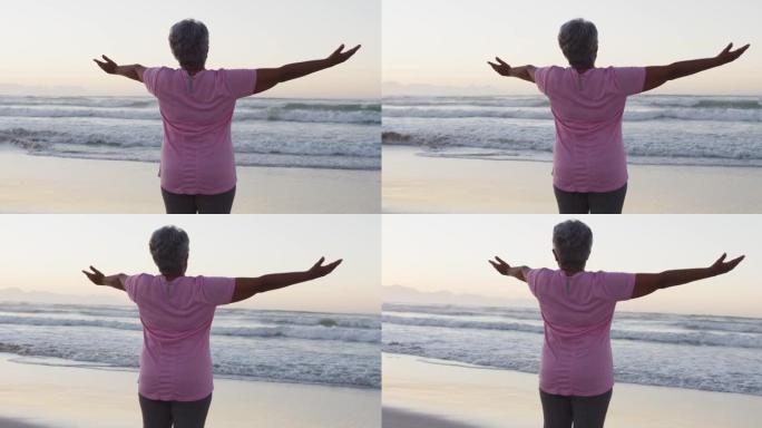 双臂张开站在海滩上的非洲裔美国高级女性的后视图