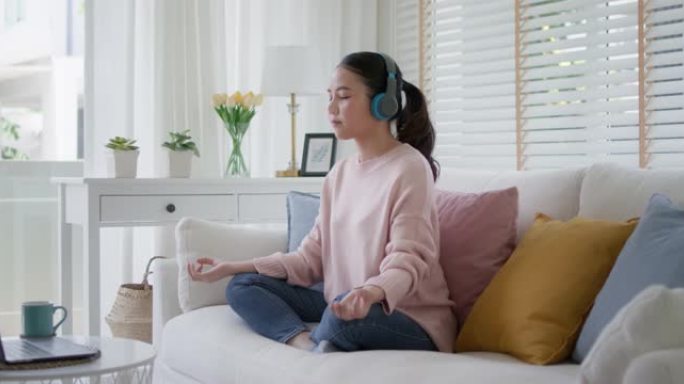 年轻的亚洲女性在家沙发上冥想轻松听音乐播客。