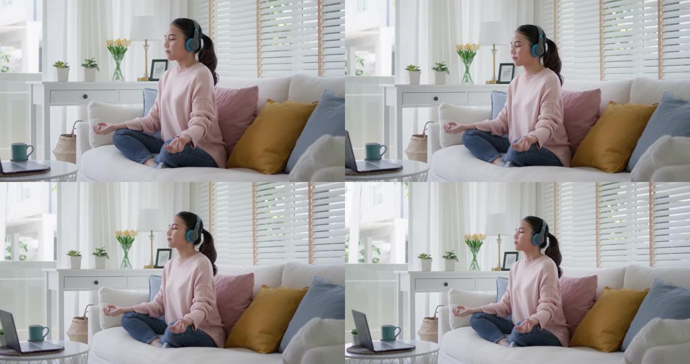 年轻的亚洲女性在家沙发上冥想轻松听音乐播客。