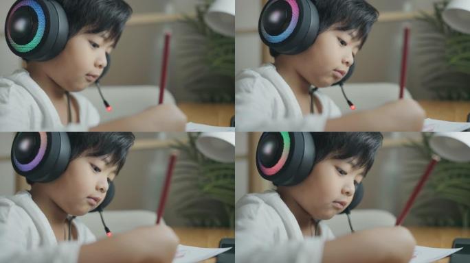 在家上学，亚洲男孩在书中写作或绘画。