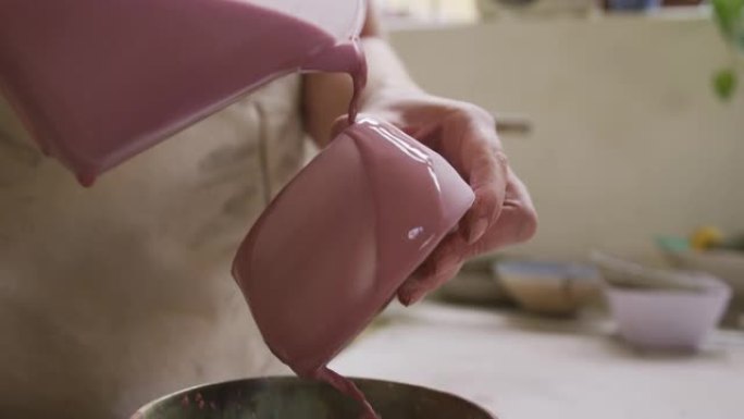 在陶器工作室，女陶工从壶上的壶中倒出油漆的特写视图