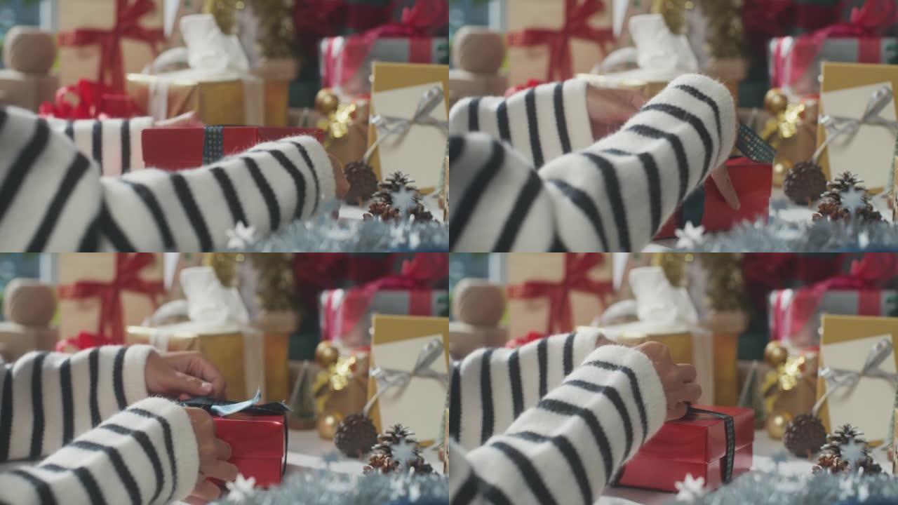 女孩双手包装礼物礼品盒的特写桌子上的冬季圣诞装饰品。