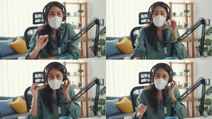 青少年亚洲女孩唱片播客使用耳机和麦克风戴口罩保护病毒看她房间里的摄像机谈话。