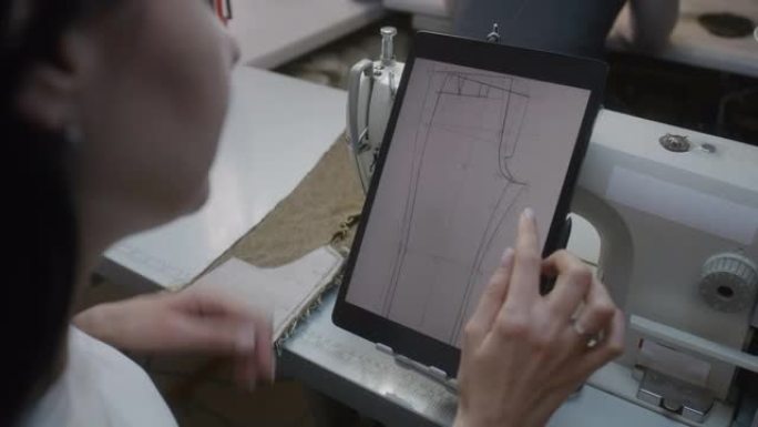女裁缝坐在缝纫机上触摸平板电脑