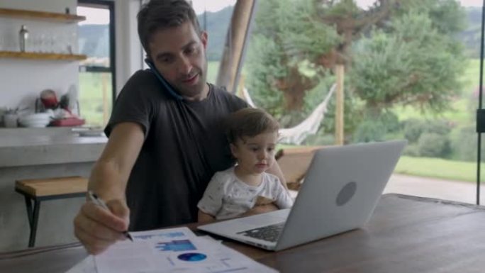 忙碌的父亲在照顾儿子的同时在家里用笔记本电脑和电话工作