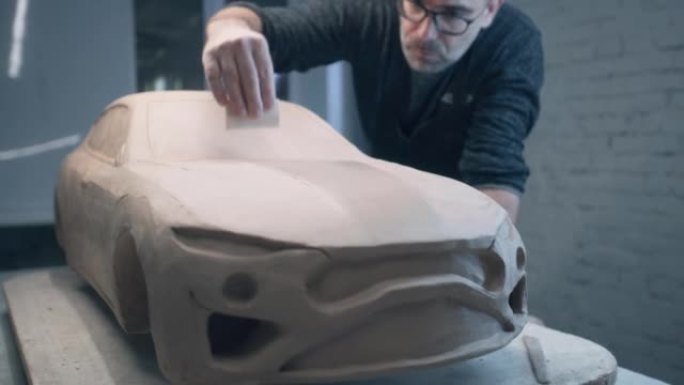 汽车设计师在用粘土制成的汽车雕塑上工作，使表面光滑