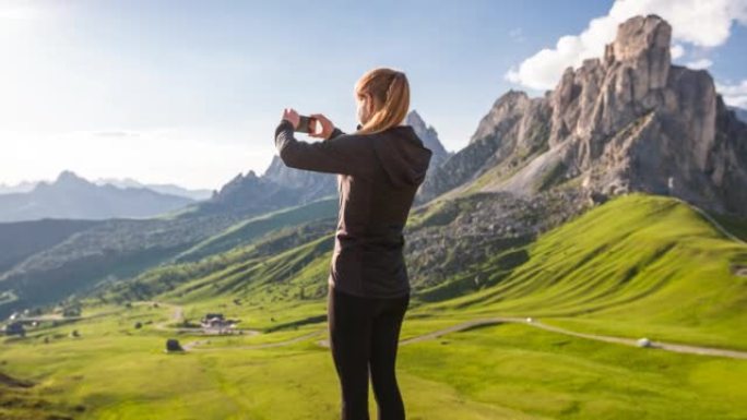 女游客在草地上俯瞰蜿蜒的山路，拍摄壮丽的景色