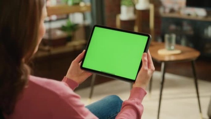 女性进行视频通话，手持平板电脑，绿屏模拟显示。在家工作时，专家会赶上同事。女人在移动设备上与朋友交谈