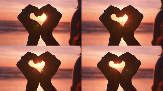女人在海滩上的爱，心和手，以争取自由，支持和幸福，在日落时签名。剪影，自然和对女孩的尊重，以浪漫，灵