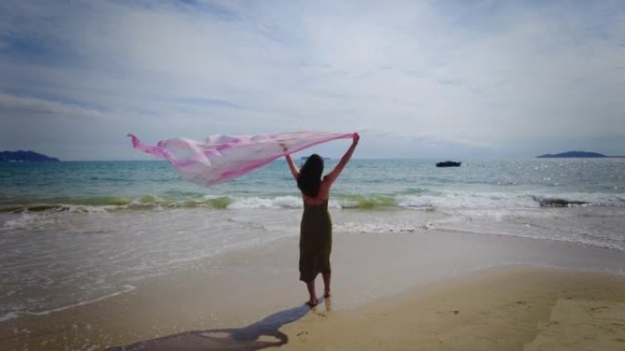 女人挥舞着围巾走在沙滩上