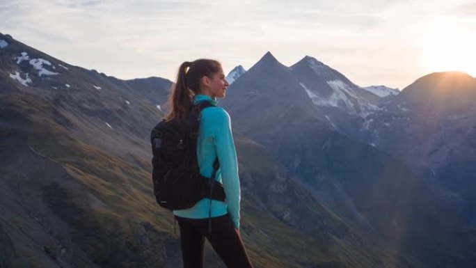 健康导向的女人站在山顶上，在日落时欣赏山峰的壮丽景色