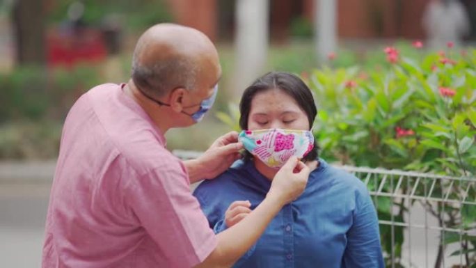 亚洲马来人退休父亲在城市街道帮助他的唐氏综合症女儿戴口罩