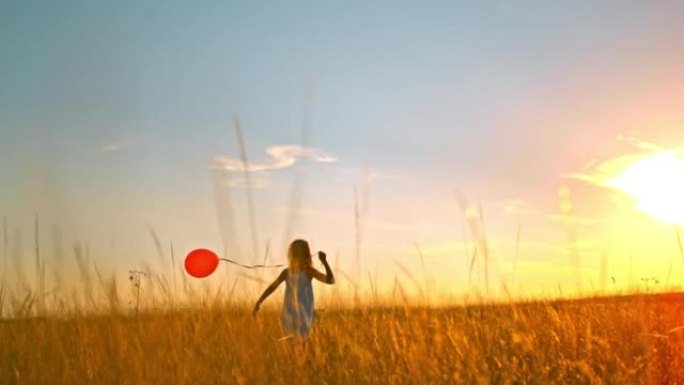 SLO MO女孩在日落时在草地上奔跑时玩红色气球