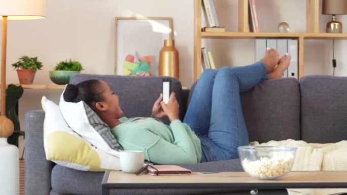 无忧无虑的女人在家里的沙发上独自放松时，在网上给她的朋友发短信和打字。一位快乐而轻松的女性在社交媒体