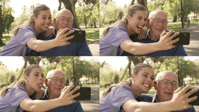 一个快乐的年轻照顾者，在外面的公园里用手机自拍时，和她的老人一起玩得很开心。中风后，坐在轮椅上的老人