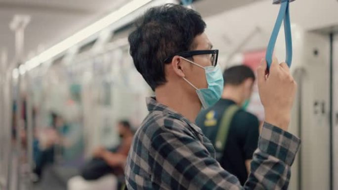 冠状病毒流行期间，年轻的亚洲男子在地铁列车上戴蓝色防护口罩。