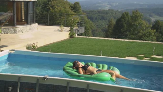 无忧无虑的白人妇女躺在叶子上漂浮，同时在自己的家庭游泳池中放松。
