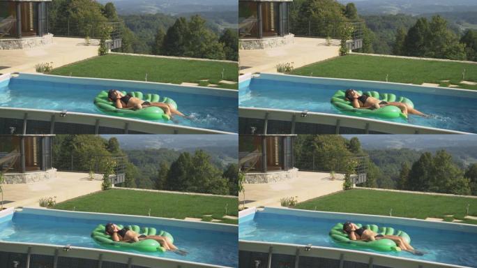 无忧无虑的白人妇女躺在叶子上漂浮，同时在自己的家庭游泳池中放松。