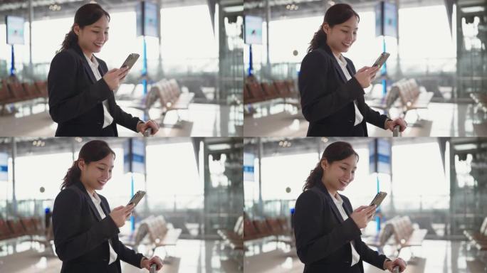 年轻的女商人在使用智能手机时穿过机场航站楼