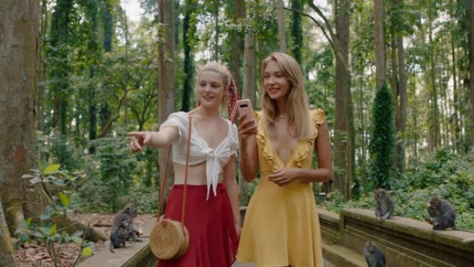 两名妇女使用智能手机在森林动物园为猴子拍照女孩朋友在手机社交媒体上分享旅行冒险发现印度尼西亚巴厘岛