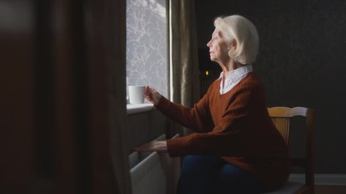 喝热饮的高级女性试图在家中通过散热器保暖，以节省生活成本能源危机