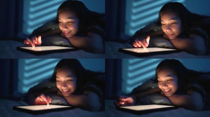 年轻的微笑女孩在家中躺在床上使用平板电脑