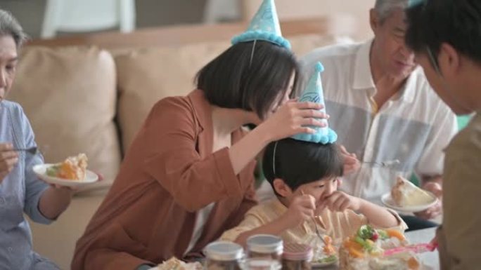 亚洲华人多代家庭庆祝生日，孙子戴着派对帽在客厅吃生日蛋糕