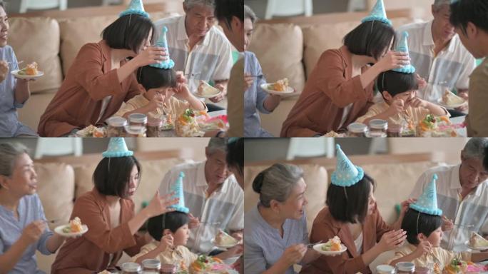 亚洲华人多代家庭庆祝生日，孙子戴着派对帽在客厅吃生日蛋糕