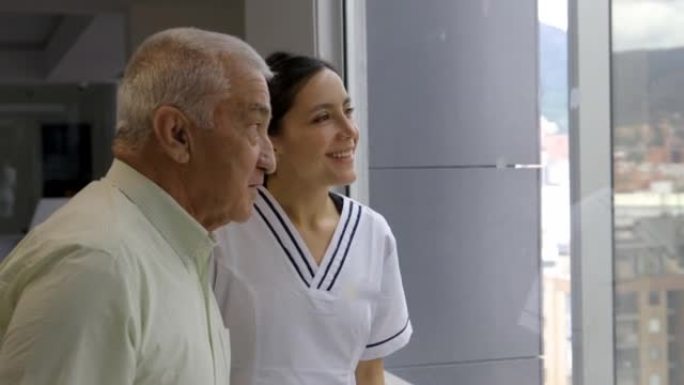爱心护士与高级患者交谈，一边在医院交谈和微笑，一边看着风景