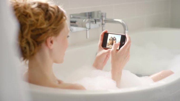 4k视频片段，一名年轻女子在泡泡浴期间浏览手机上的照片