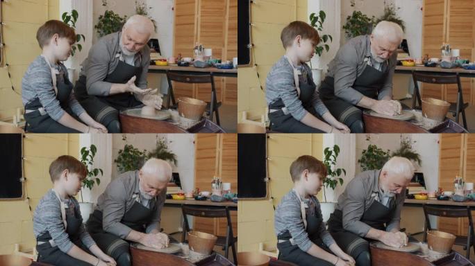 可爱的男孩在陶器工作室和高级祖父聊天，用抛掷轮制作陶瓷