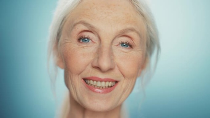 美丽的高级女人转身的特写肖像，看着相机，笑容灿烂。华丽的老年女士，自然郁郁葱葱的灰色头发，蓝色的眼睛