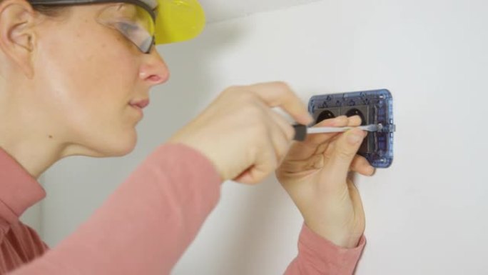 特写: 女人在安装电源插座时将螺丝拧入墙壁