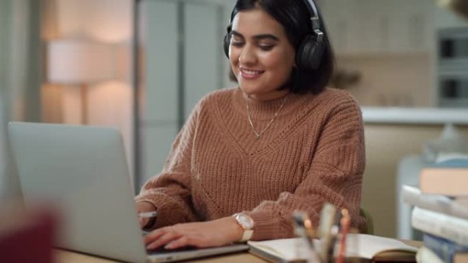 4k视频片段，一个迷人的年轻女子独自坐在家里，戴着耳机使用笔记本电脑