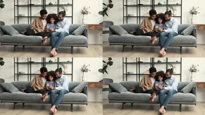 非洲夫妇和女儿使用现代智能手机在沙发上放松