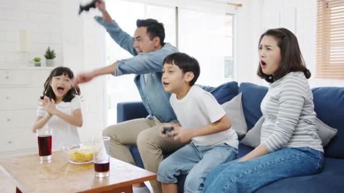 快乐亚洲家庭爸爸，妈妈和孩子们在家里的客厅用技术控制台有趣地玩视频游戏。