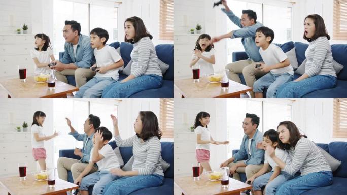 快乐亚洲家庭爸爸，妈妈和孩子们在家里的客厅用技术控制台有趣地玩视频游戏。
