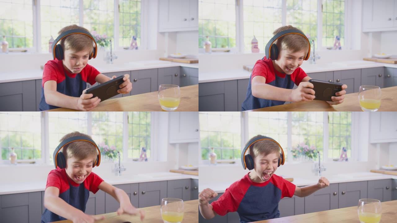 家里的男孩在厨房玩手机游戏戴着无线耳机
