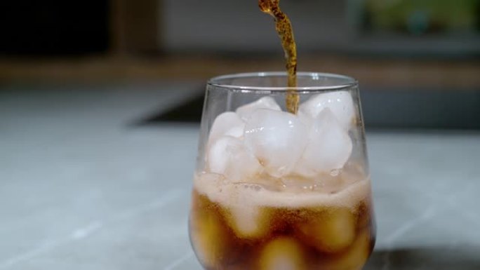 特写: 苏打水倒在融化在优雅玻璃杯中的冰块上。