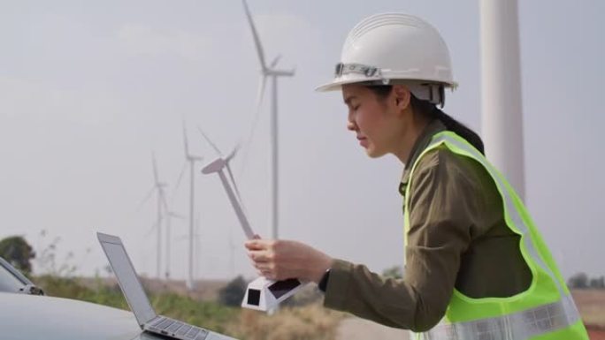 戴着安全帽的女工程师在风力涡轮机前使用数字平板电脑。清洁可再生绿色风力发电概念。