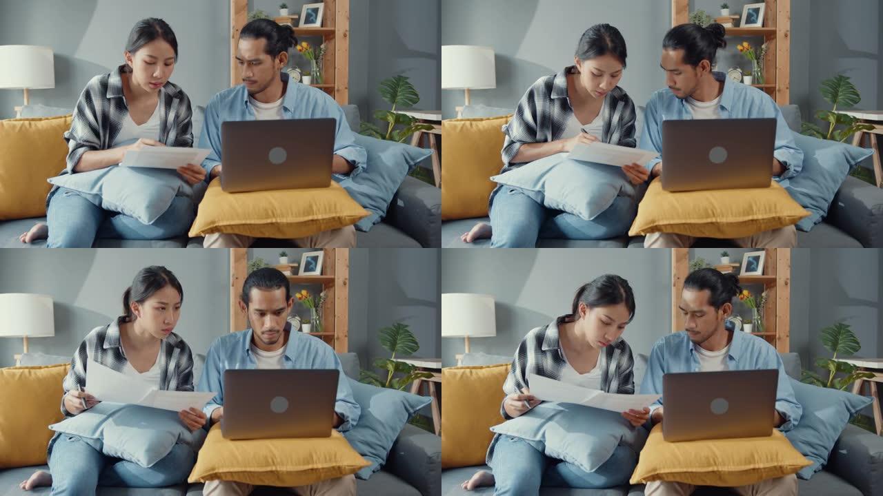 亚洲年轻夫妇坐在沙发上认真关注笔记本电脑检查文件纸质支付账单在线计划客厅预算费用。