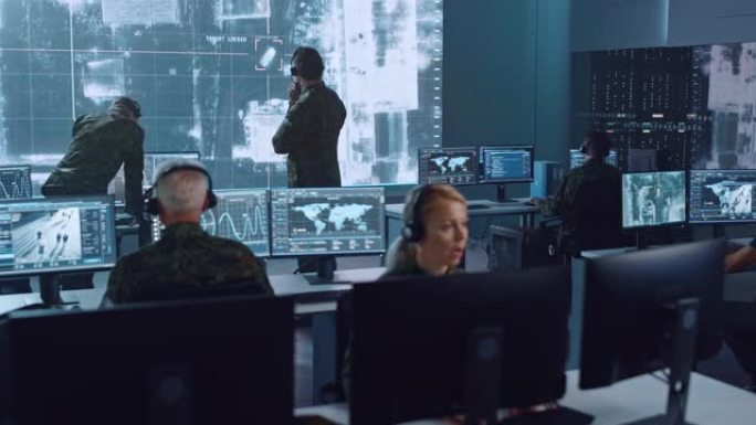 军事监视小组的人员将目标锁定在卫星上的车辆上，并在办公室的大型显示器上对其进行监视，以进行网络操作，