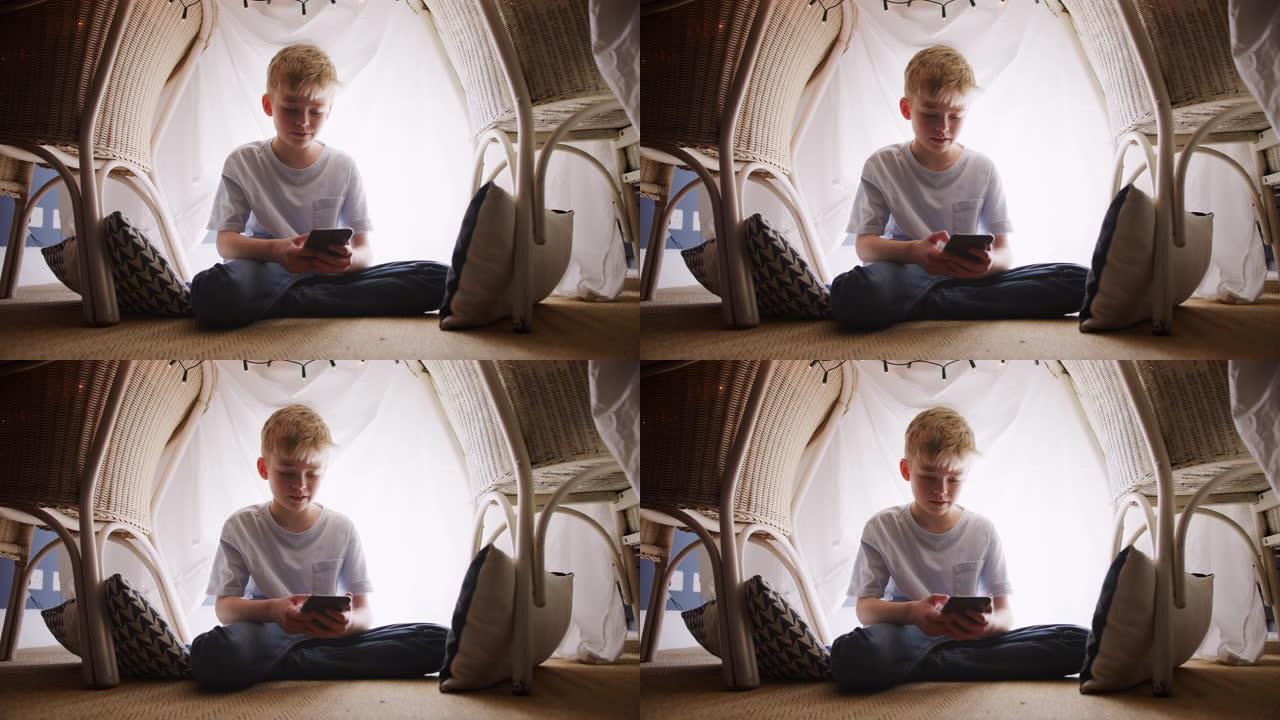 坐在书房或营地里的男孩在家里玩手机