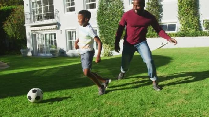 在阳光明媚的日子里，非洲裔美国父亲和儿子在花园里一起踢足球