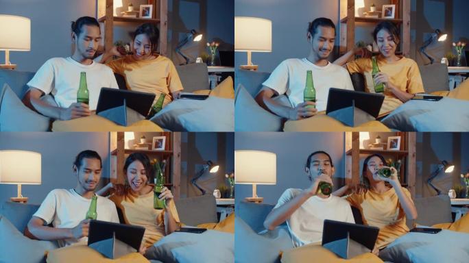 快乐的年轻亚洲夫妇享受夜间派对活动在线坐沙发使用平板电脑视频通话与朋友在家里的客厅通过视频通话吐司喝