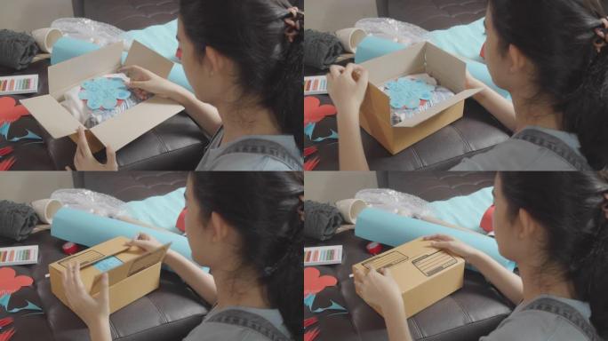 俯视图亚洲年轻少女制作手工物品护理包。可爱的女孩打包一个包装箱，准备从远处寄给她的家人或朋友。