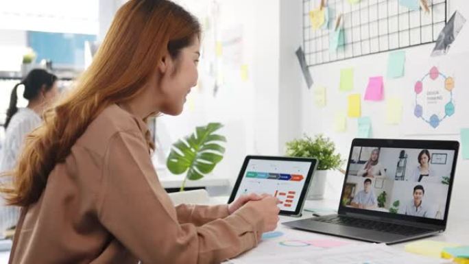 使用笔记本电脑的亚洲商人与同事交谈，讨论有关新普通办公室视频通话会议计划的商业头脑风暴。