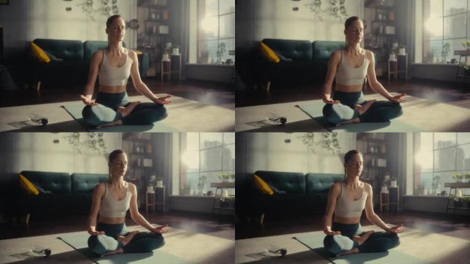 运动的年轻女性锻炼身体，早上在家里阳光明媚的房间里练习冥想。穿着运动服的美女在瑜伽垫上练习正念。