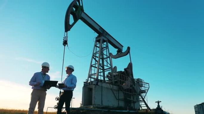 油井，原油，钻机，油田，原油价格，油气，油桶，石油工业概念。两名工程师在抽油机旁边交谈