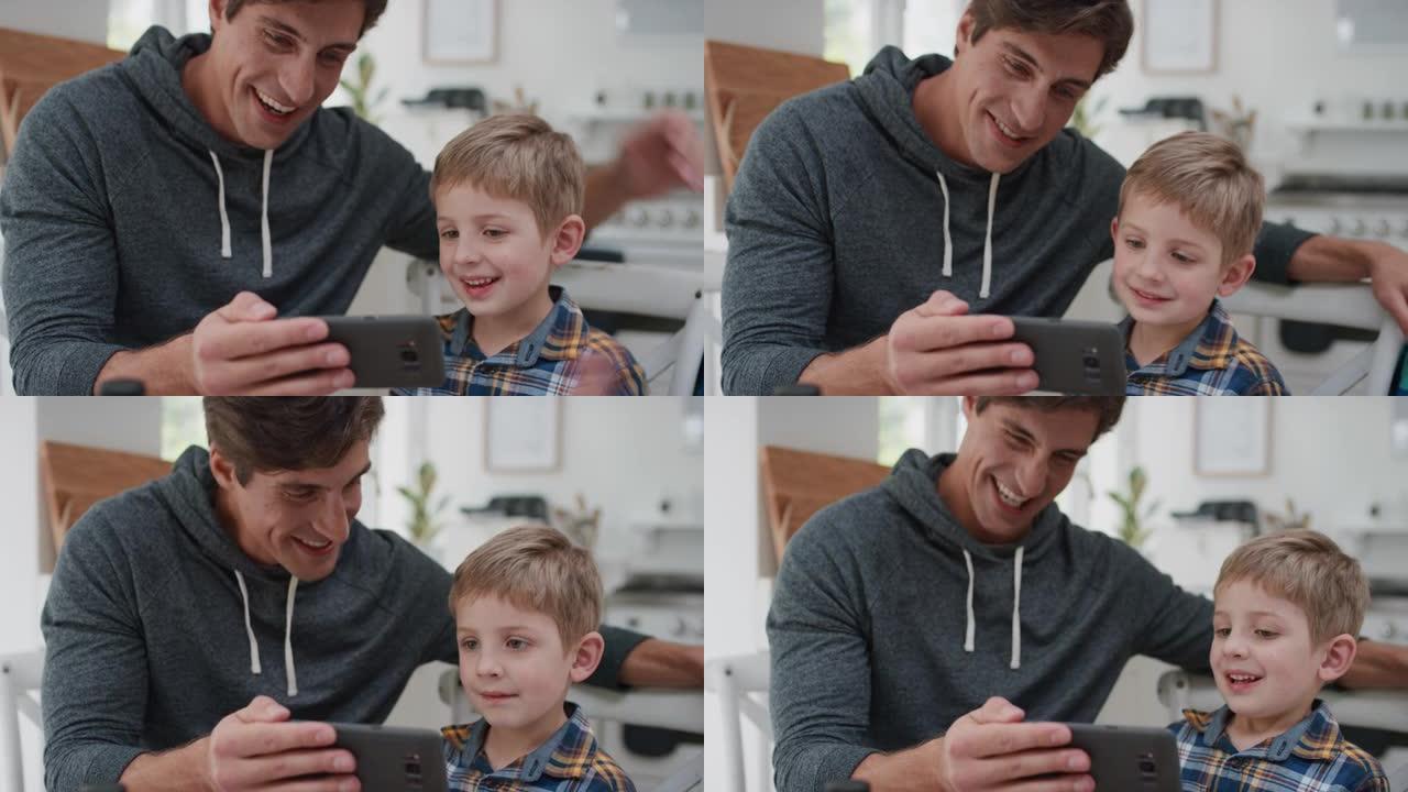 父子俩用智能手机看手机在线娱乐快乐小男孩在家和爸爸一起开心放松4k镜头